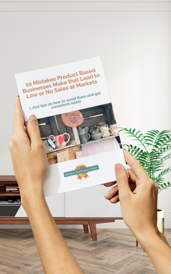 2 hands holding the booklet titled 10 Mistakes Product Based Businesses Make That Lead to Low or No Sales At Markets"